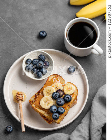 Peanut butter toast with banana and blueberry on a plate on a dark  background with a cup of coffee 122907552
