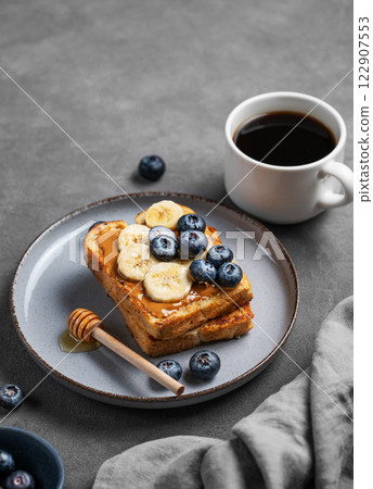 Peanut butter toast with banana, blueberry and honey on a plate on a dark background Peanut butter toast with banana, blueberry and honey on a plate on a dark background 122907553