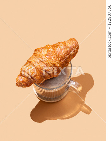 Fresh croissant on a cup of cappuccino or latte on an orange background with shadow. Fresh croissant on a cup of cappuccino or latte on an orange background with shadow. 122907556