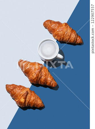 Fresh croissants and a cup of cappuccino or latte coffee lie diagonally on a blue background 122907557