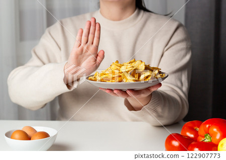 Woman saying "NO" to chips. Hand sign to refuse junk food. Choosing healthy eating. Trying eat vegetables. Healthy nutrition for weight loss. 122907773
