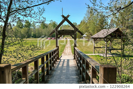 Scenic wooden bridge leading to a rustic wooden gate in a peaceful countryside landscape. 122908264