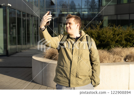 Portrait handsome young man taking selfie on urban background. 30s man using phone outdoors. Smiling businessman walking in urban area. Urban lifestyle concept. Spring time. 122908894