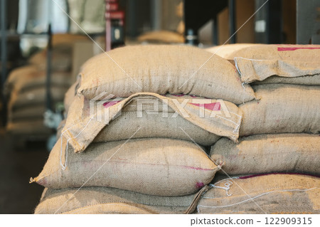 Stacked burlap sacks filled with goods in a warehouse. Industrial storage of agricultural or food products in traditional fabric bags. Supply chain, logistics concept 122909315