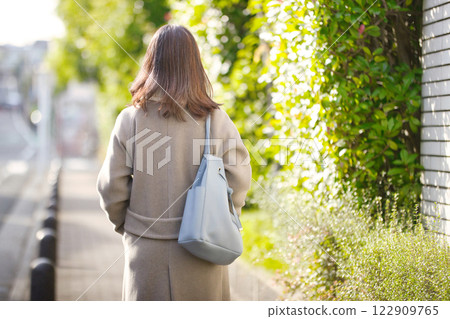 Back view of a middle-aged woman walking in the city wearing a coat 122909765