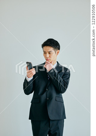 A young man in his twenties holding a smartphone with his hand on his chin 122910506