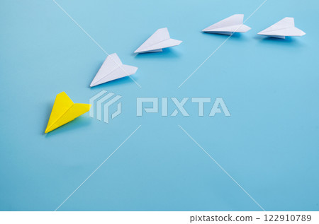 Side view of yellow paper airplane origami leading other white airplanes on blue background with customizable space for text. Business and Leadership skills concept. 122910789