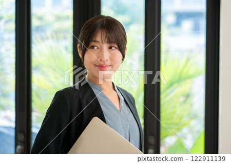 A smiling Japanese woman standing by the window with a laptop A smiling Japanese woman standing by the window with a laptop 122911139