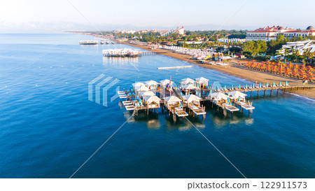 Aerial view of a luxury beach resort with private cabanas on wooden piers over the sea. 122911573