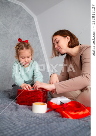 Mid shot of mother and daughter together packing a Valentine's Day and Mother's day gift. Caucasian woman and little girl are preparing for the holiday. Vertical 122912127