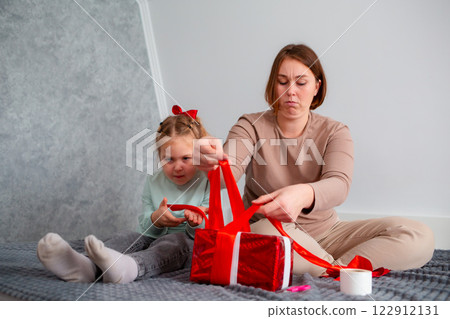 Wide shot of adult mother and her daughter pack a gift together for Valentine's Day and Mother's Day. Caucasian woman and a cute little girl spend time together 122912131