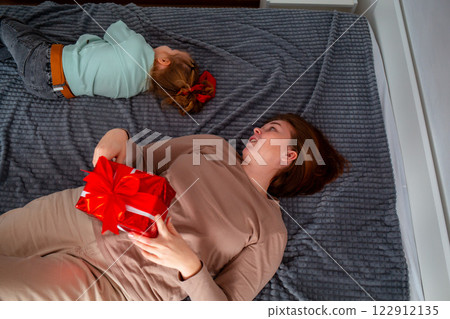 Top view of Caucasian adult mother and little girl are lying on bed with gift in their hand. Happy family leisure. Concept of Mother's day 122912135