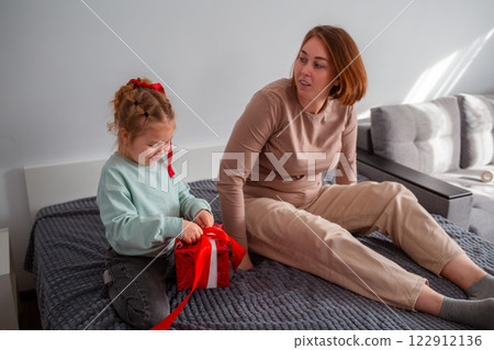 Mid shot of young Caucasian mother and her daughter pack a festive gift, sitting on the bed. The concept of Valentine's Day and Mother's Day 122912136