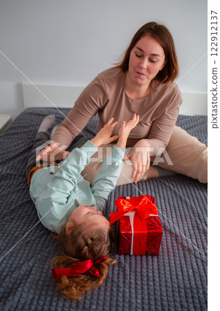 Vertical orientation of young Caucasian woman lies with her daughter. The girl prepared a gift for her mother for the holiday. The concept of family time 122912137