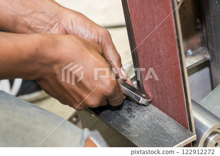 The hand deburring the metal parts with sandpaper belt by skill operator. 122912272