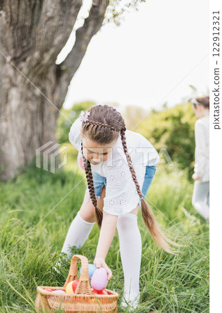 Easter egg hunt. Girl child Wearing Bunny Ears Running To Pick Up Egg In Garden. Easter tradition. Baby with basket full of colorful eggs. Bunny in basket 122912321