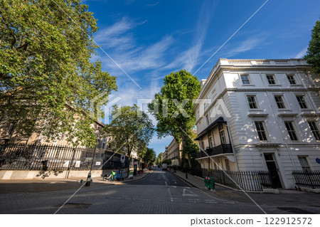 A small street in England, surrounded by buildings, fences, and trees, creating a quaint and charming atmosphere. A small street in England, surrounded by buildings, fences, and trees, creating a quaint and charming atmosphere. 122912572