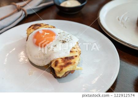 A fried sunny-side-up egg topped with black pepper sits beautifully on melted cheese toast, served on a white plate. Perfect for promoting breakfast menus, cafes, or food blogs. A fried sunny-side-up egg topped with black pepper sits beautifully on melted cheese toast, served on a white plate. Perfect for promoting breakfast menus, cafes, or food blogs. 122912574
