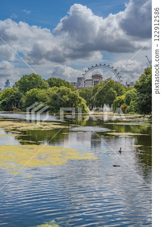 A tranquil pond in Public Park with lush greenery in the foreground, while the Iconic landmark and surrounding buildings are visible in the background. 122912586