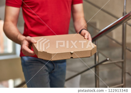 delivery man in red t-shirt holding pizza box on the stairs delivery man in red t-shirt holding pizza box on the stairs 122913348