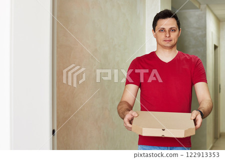 handsome delivery man in red t-shirt giving food order, holding pizza box standing at doorway, copy space handsome delivery man in red t-shirt giving food order, holding pizza box standing at doorway, copy space 122913353