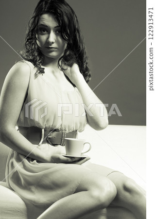 woman sitting on sofa holds coffee cup woman sitting on sofa holds coffee cup 122913471