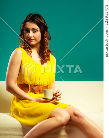 woman sitting on sofa holds coffee cup 122913472