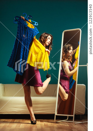 woman shopper holds hangers with clothes looking in mirror woman shopper holds hangers with clothes looking in mirror 122913540