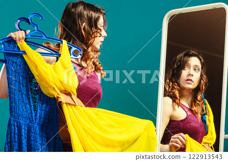 woman shopper holds hangers with clothes looking in mirror 122913543