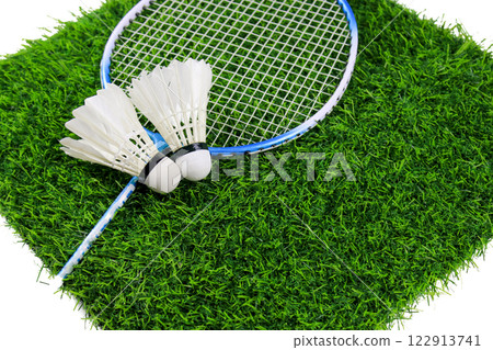 White shuttlecocks and badminton racket rest on artificial grass, outdoor sports and recreation. 122913741