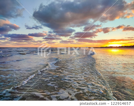 Golden sunset reflects on the ocean waves, creating a tranquil atmosphere with colorful clouds 122914657