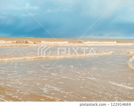 Gentle waves lap against the sandy beach as dark clouds hover overhead in the late afternoon light 122914669
