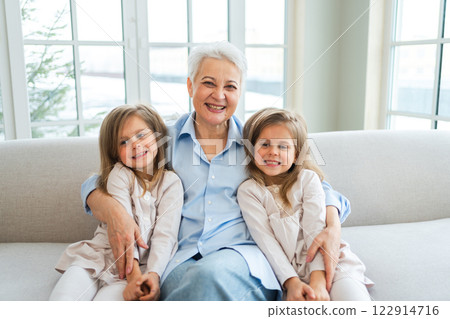 Happy family at home. Two little girls sisters twins grandmother enjoying time together. Good time at home. Grandma granddaughters child kids emotional bonding hugging together. Family generations Happy family at home. Two little girls sisters twins grandmother enjoying time together. Good time at home. Grandma granddaughters child kids emotional bonding hugging together. Family generations 122914716