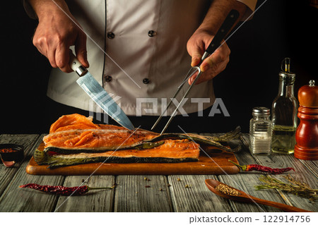A skilled chef slices through a beautifully cooked piece of salmon on a wooden cutting board. Service concept for a restaurant or hotel A skilled chef slices through a beautifully cooked piece of salmon on a wooden cutting board. Service concept for a restaurant or hotel 122914756