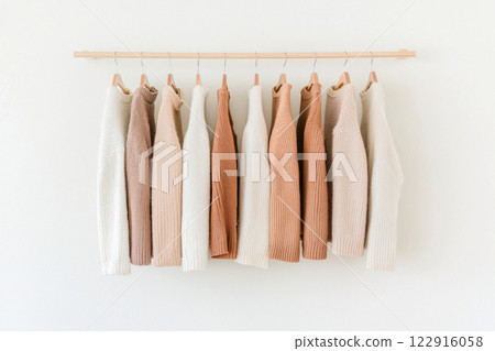 Elegant collection of soft, neutral-colored sweaters hanging on a minimalist rack. 122916058