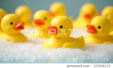 Photograph of a group of bright yellow toy rubber duckies swimming in soapy white bubble foam in a bathtub with room for text. 122916115