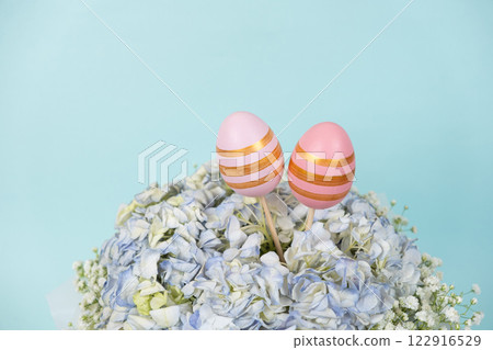 Two Easter painted eggs in a bouquet of flowers on a blue background, copy space for text 122916529