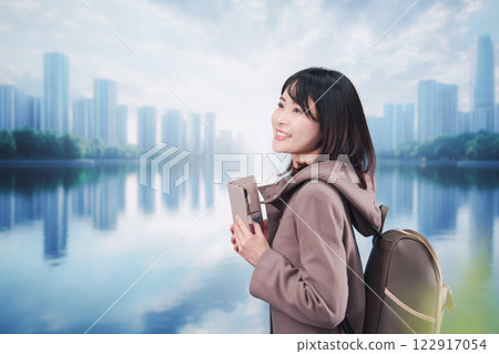 A young woman wearing a coat and walking outside while using a smartphone 122917054