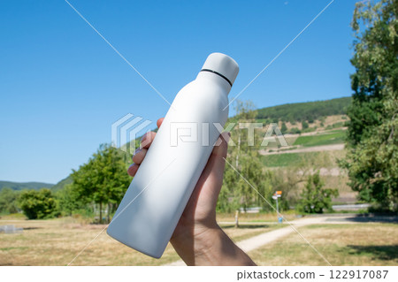 Man holding in the hand white thermo stainless bottle with refreshing water on the nature. 122917087