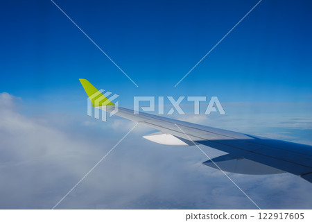 View of an airplane wing featuring a bright green wingtip, captured mid flight with a clear blue sky and scattered clouds visible below. 122917605