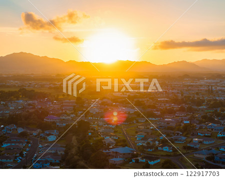 Aerial view of a residential area on Kauai island during sunset, with mountains in the background, lush greenery, and scattered clouds in the sky. 122917703