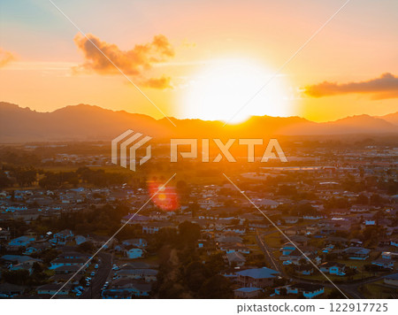 A vibrant sunset illuminates the sky over a residential area on Kauai island, with golden hues, scattered clouds, and mountains in the background. A vibrant sunset illuminates the sky over a residential area on Kauai island, with golden hues, scattered clouds, and mountains in the background. 122917725