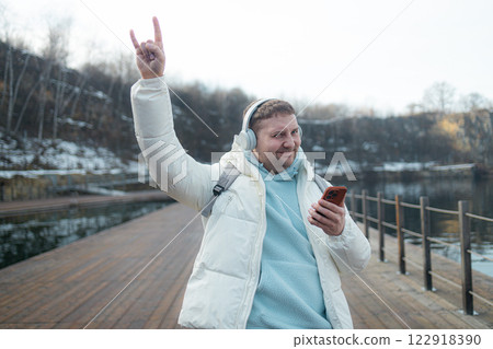 Happy guy walking and using a smart phone to listen music with headphones in a winter Happy guy walking and using a smart phone to listen music with headphones in a winter 122918390