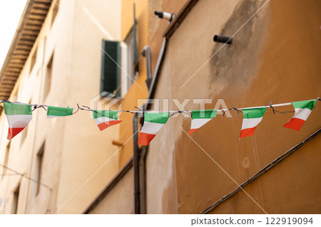 Typical street with houses in Italy. Facade of a yellow building with Italian flags. Italian flag in an old town narrow street of a city in Italy Typical street with houses in Italy. Facade of a yellow building with Italian flags. Italian flag in an old town narrow street of a city in Italy 122919094