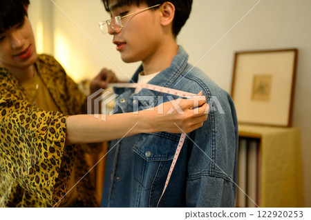 Tailor measuring a client shoulder with measuring tape for custom clothing Tailor measuring a client shoulder with measuring tape for custom clothing 122920253