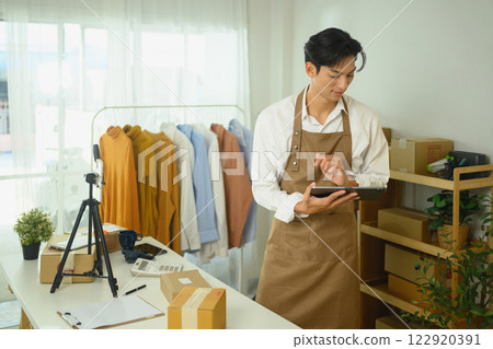 An online store owner checking orders on digital tablet while standing in a workspace 122920391