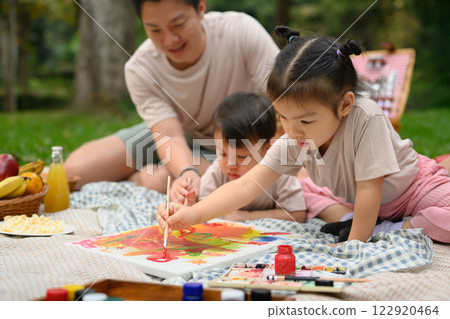 Two little children painting while enjoying a family picnic in the park 122920464