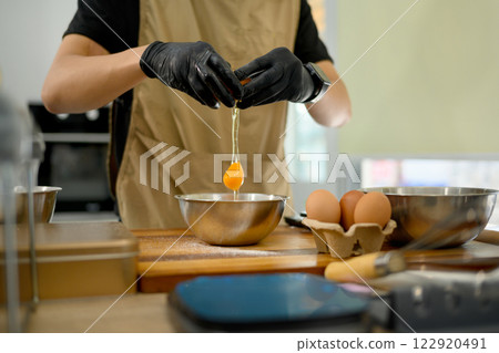 Male baker cracking an egg into mixing bowl preparing ingredients for homemade cookies 122920491