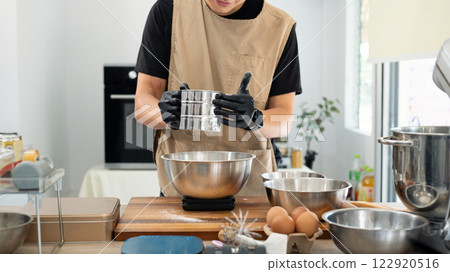 Male baker sifting flour for chocolate chip cookies dough over kitchen counter 122920516