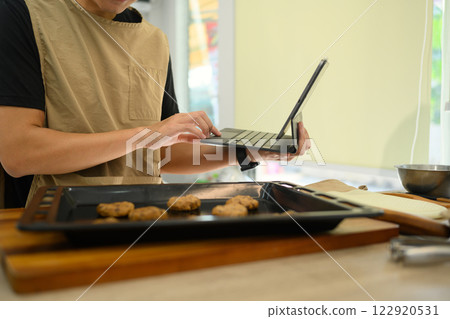 Smiling male baker checking recipe on digital tablet while preparing chocolate chip cookies Smiling male baker checking recipe on digital tablet while preparing chocolate chip cookies 122920531